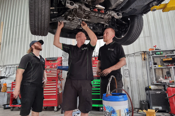 3 mechanics working on a raised cars underbody